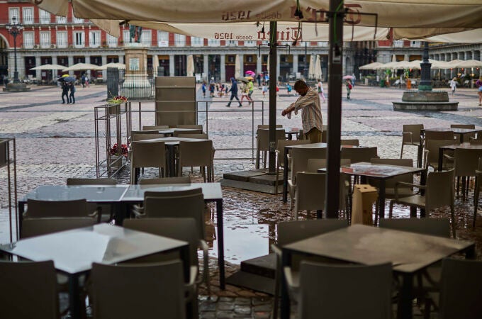 Ambiente de lluvia en las terrazas de la Plaza Mayor de Madrid. un camarero limpia las mesas
