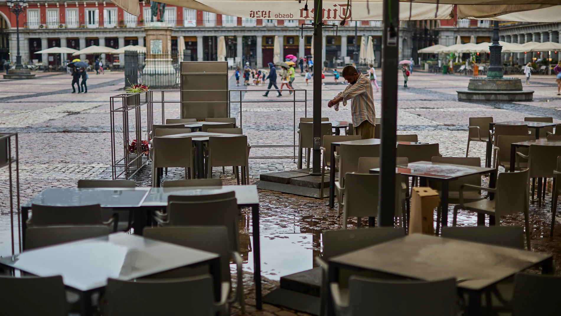 Ambiente de lluvia en las terrazas de la Plaza Mayor de Madrid. un camarero limpia las mesas