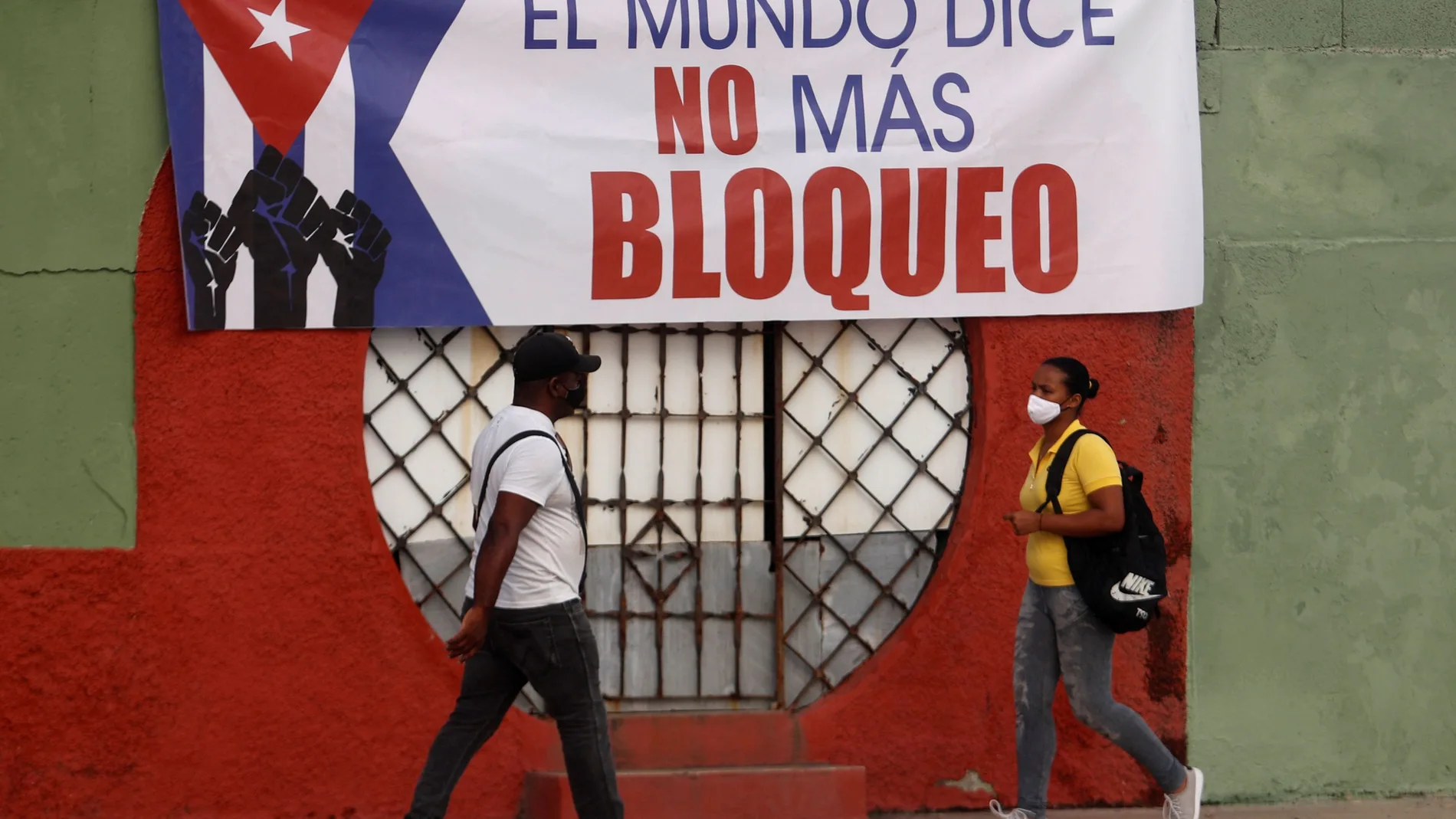 Fotografía del 20 de junio que muestra a dos personas que caminan frente a un cartel contra el bloqueo de Estados Unidos a la isla