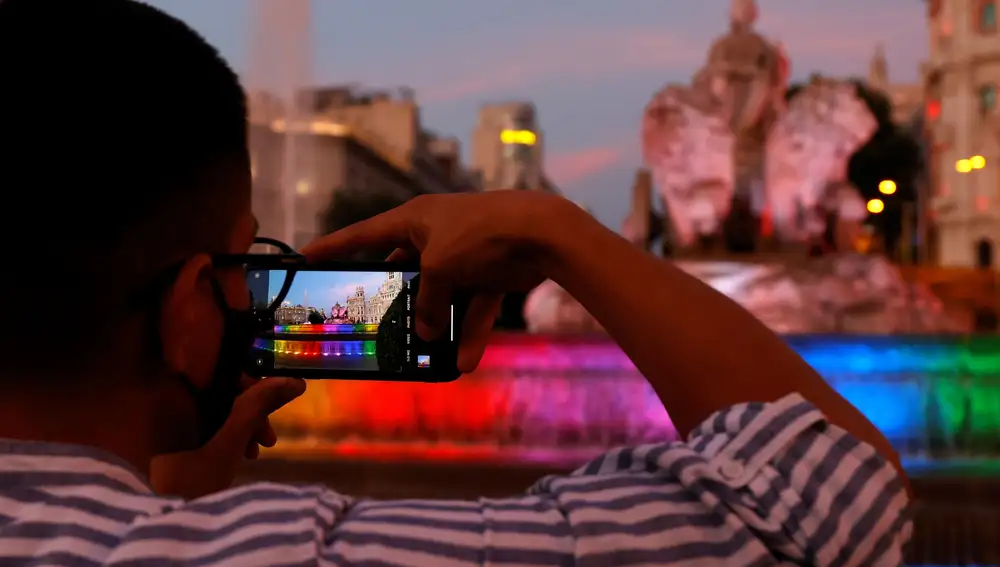 GRAF8117. MADRID, 25/06/2021.- Un hombre fotografía la fuente de Cibeles, que aparece iluminada con los colores de la bandera LGTBI con motivo del inicio de la fiestas del Orgullo 2021. EFE/Mariscal