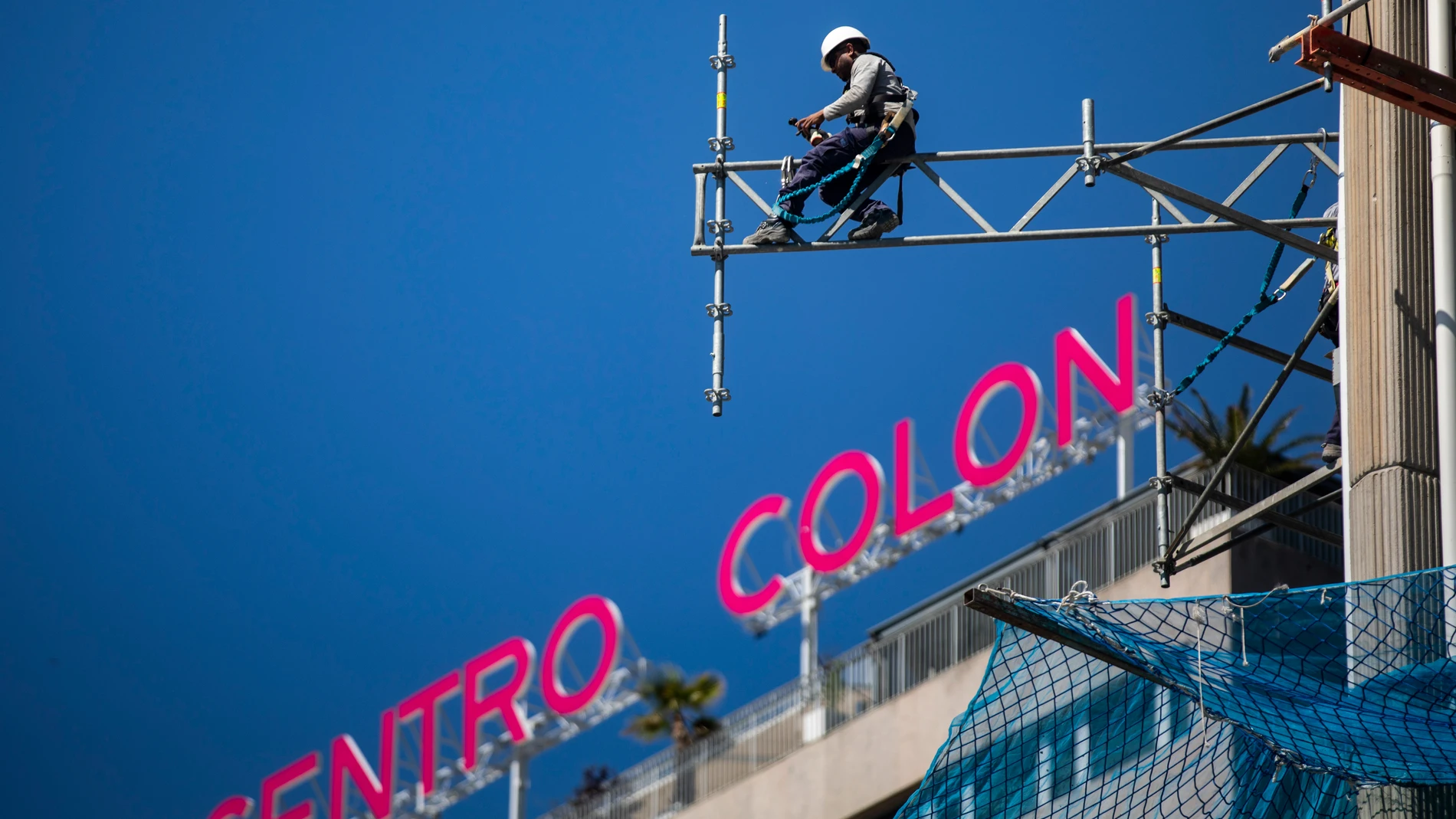 Imagen de unos operarios desmontando andamios en las Torres de Colón con la letras del edificio Centro Colon a la espalda