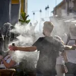 Un chico se refresca del calor con un difusor de vapor de agua de un restaurante