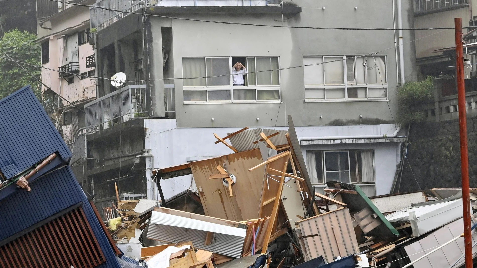Un vecino mira por la ventana los daños causados por las fuertes lluvias en el distrito de Izusan, en Atami, Japón