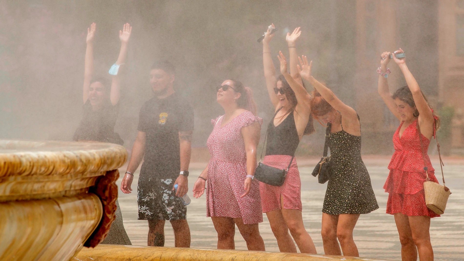 Unos turistas se refrescan con el agua que desprende la fuente de la Plaza de España de Sevilla. EFE/Julio Muñoz