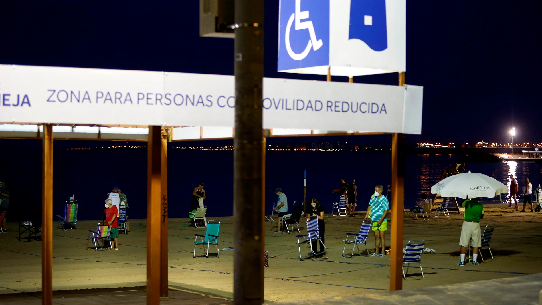 Varias personas colocan sus sillas de playa para coger sitio en alguna de las parcelas, tras hacer cola de madrugada en una playa de Torrevieja este sábado