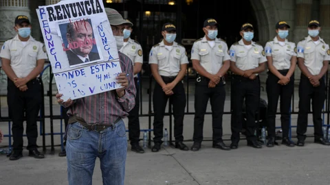 A protestors holds a sign with a portrait of Guatemalan President Alejandro Giammattei outside the National Palace as people attend a rally in support of anti-corruption prosecutor Juan Francisco Sandoval, in Guatemala City, Saturday, July 24, 2021. Sandoval fled Guatemala late Friday, arriving in neighboring El Salvador just hours after he was removed from his post. (AP Photo/Moises Castillo)