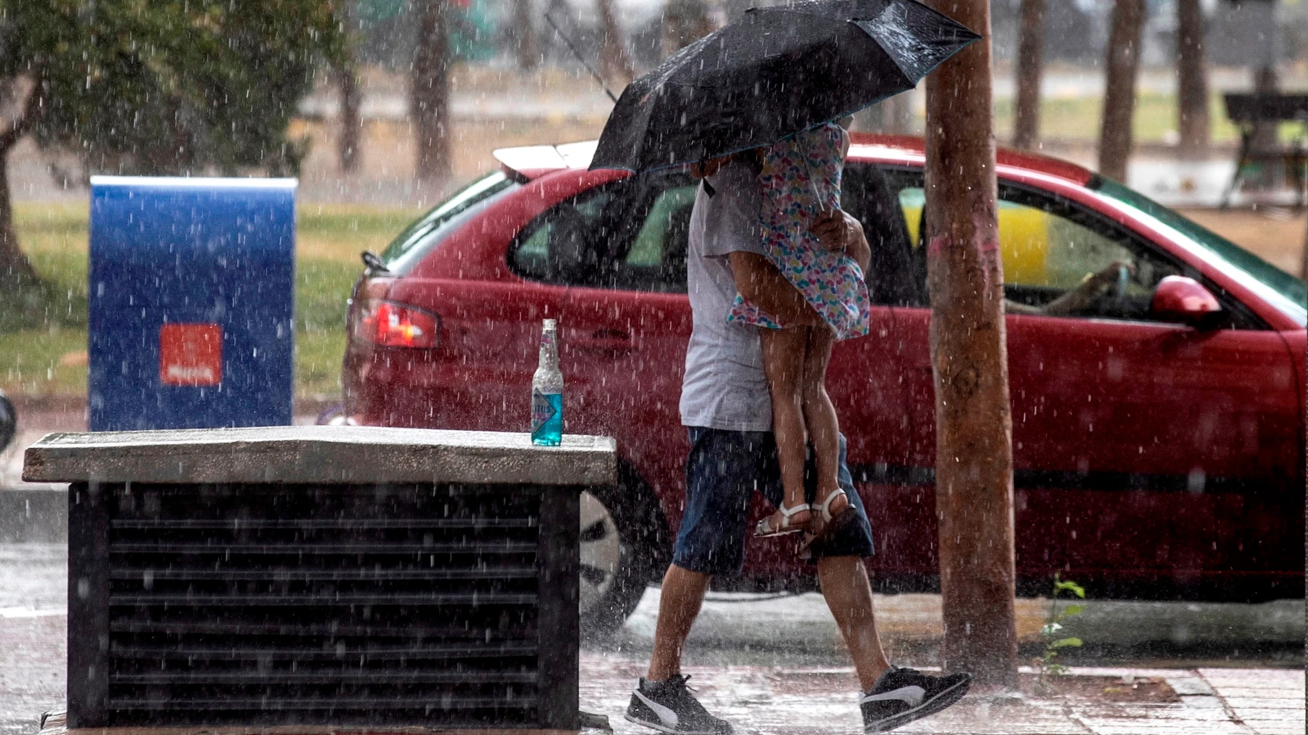 Un hombre protege con un paraguas a su hija de la lluvia en Ronda Sur, Murcia, el pasado lunes