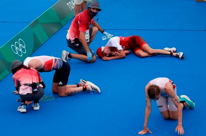 Jonathan Brownlee (i) de Gran Bretaña, Max Studer (c) de Suiza y Casper Stornes de Noruega descansan en el suelo tras cruzar la meta del triatlón masculino durante los Juegos Olímpicos 2020