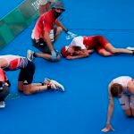 Jonathan Brownlee (i) de Gran Bretaña, Max Studer (c) de Suiza y Casper Stornes de Noruega descansan en el suelo tras cruzar la meta del triatlón masculino durante los Juegos Olímpicos 2020