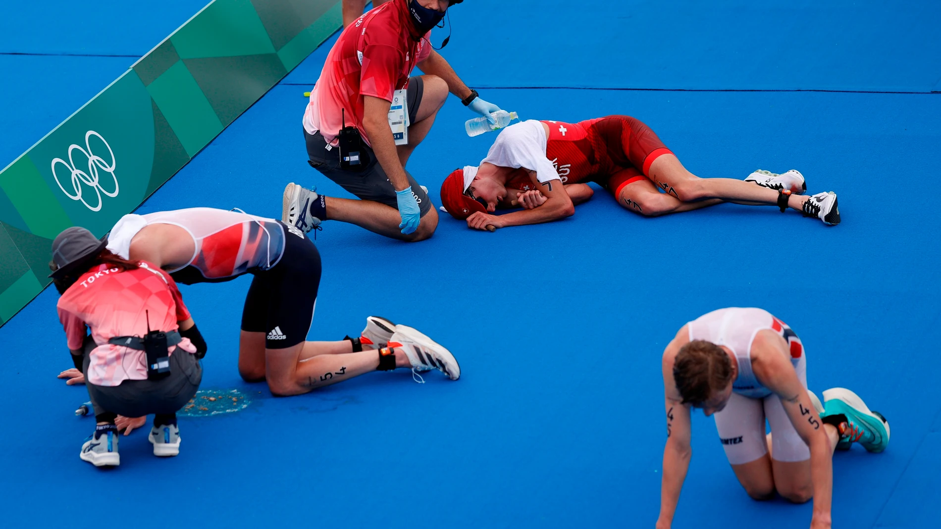Jonathan Brownlee (i) de Gran Bretaña, Max Studer (c) de Suiza y Casper Stornes de Noruega descansan en el suelo tras cruzar la meta del triatlón masculino durante los Juegos Olímpicos 2020