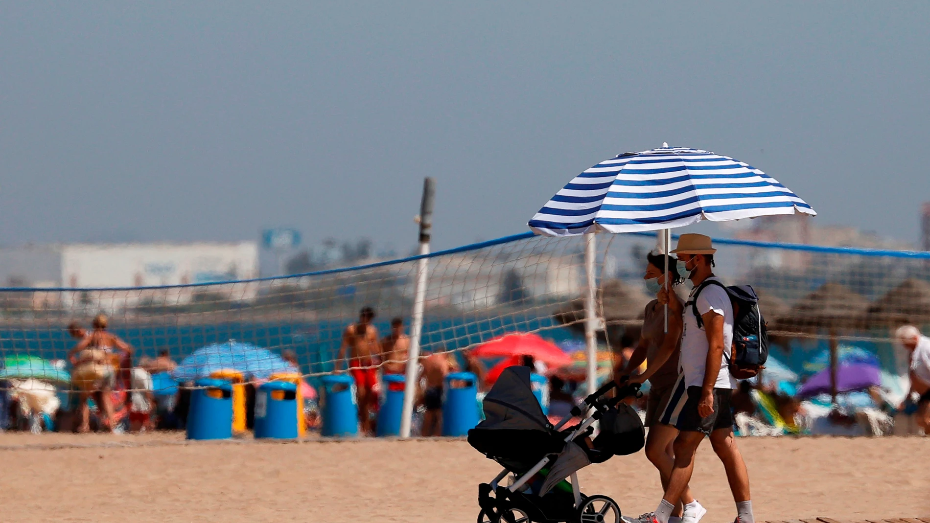 Dos personas caminan por una pasarela de la playa de La Malvarrosa de Valencia protegiéndose del intenso sol con una sombrilla. La Agencia Estatal de Meteorología (Aemet) ha establecido para este jueves alerta amarilla. Foto de archivo