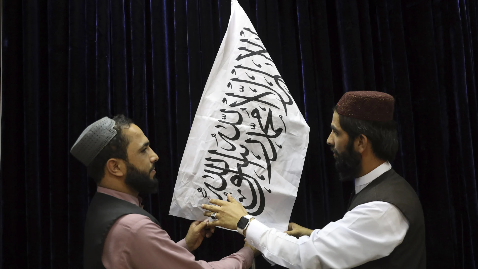Oficiales talibanes arreglan la bandera antes de una rueda de prensa en Kabul