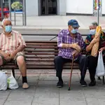 Imagen de tres personas mayores sentadas en un banco con bolsas de compra