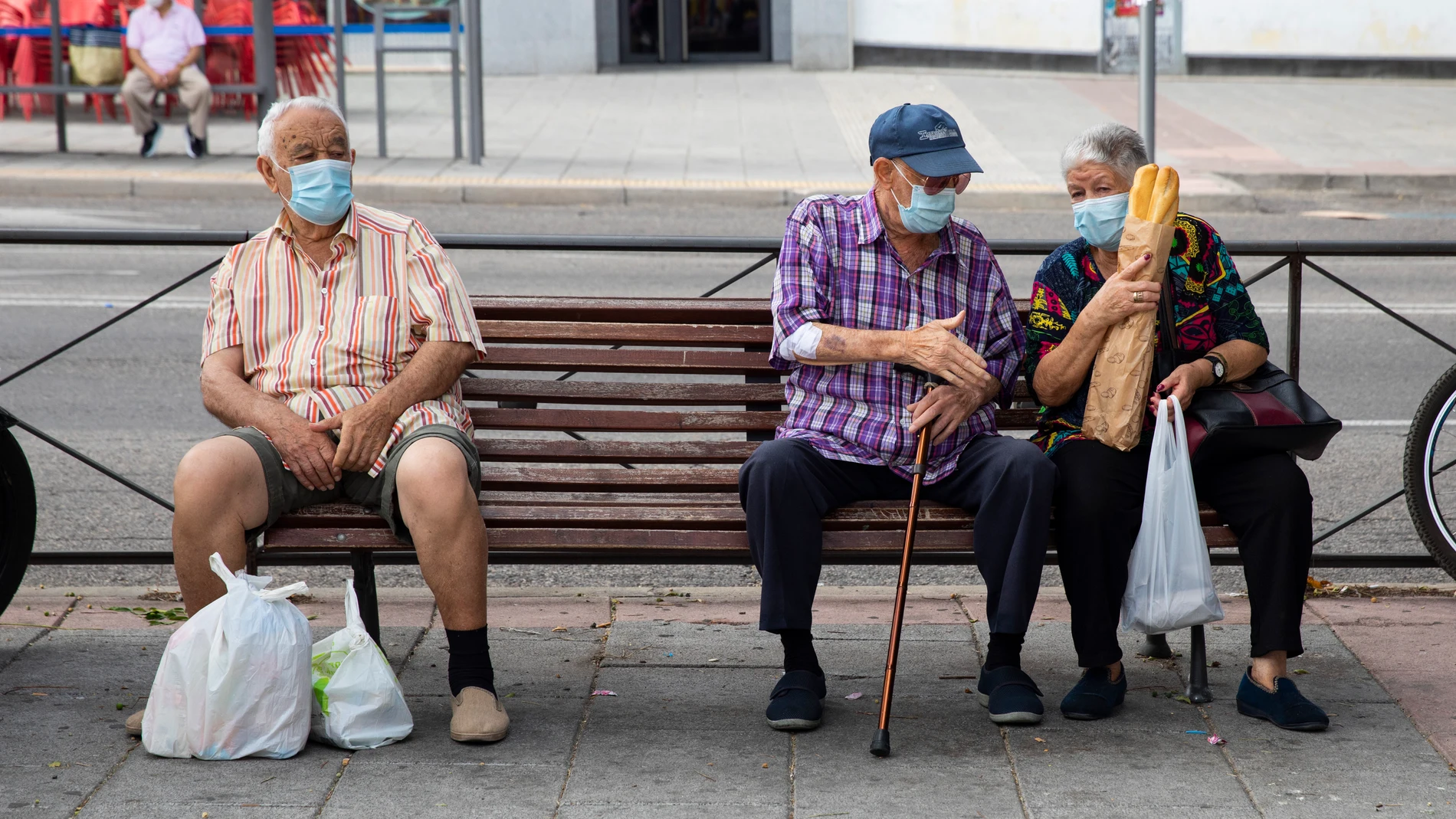 Imagen de tres personas mayores sentadas en un banco con bolsas de compra