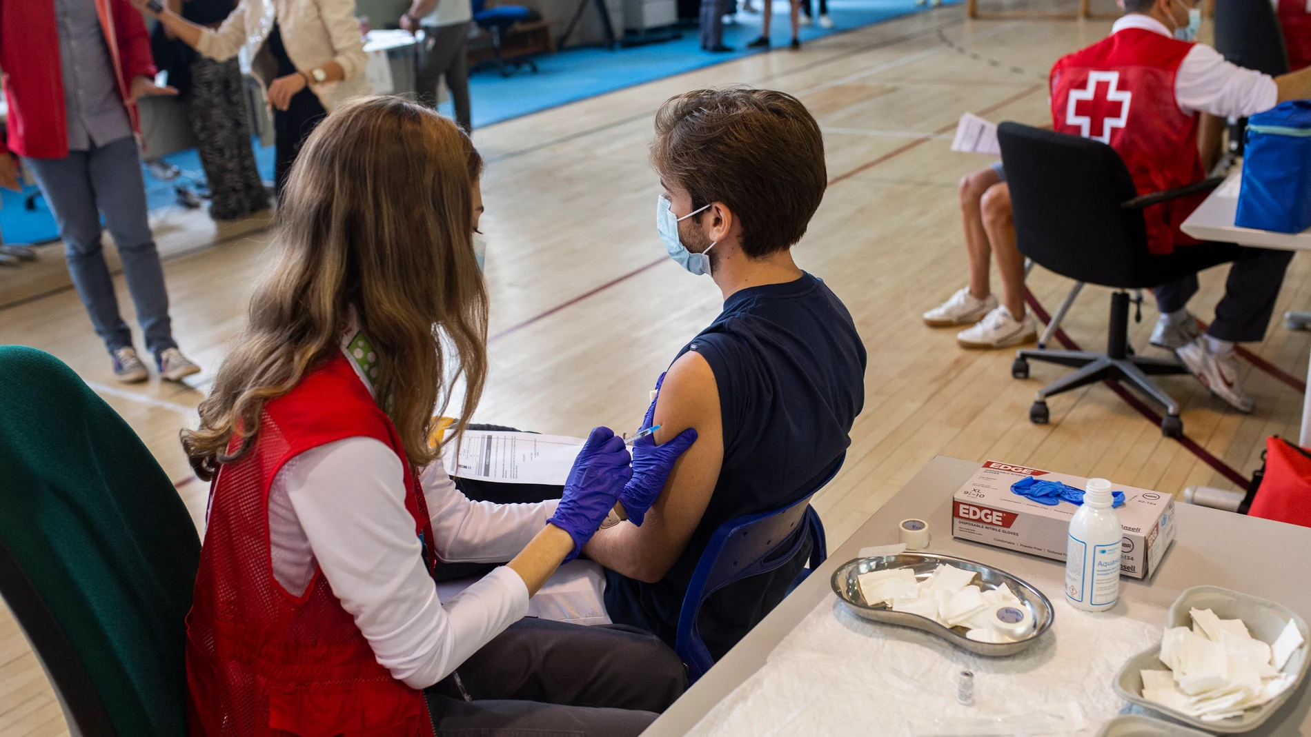 Una voluntaria de Cruz Roja administra una dosis de la vacuna a un estudiante universitario en el campus de Ciudad Universitaria de Madrid