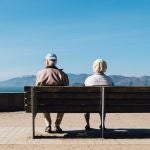 Dos ancianos sentados en un banco mirando hacia el horizonte costero