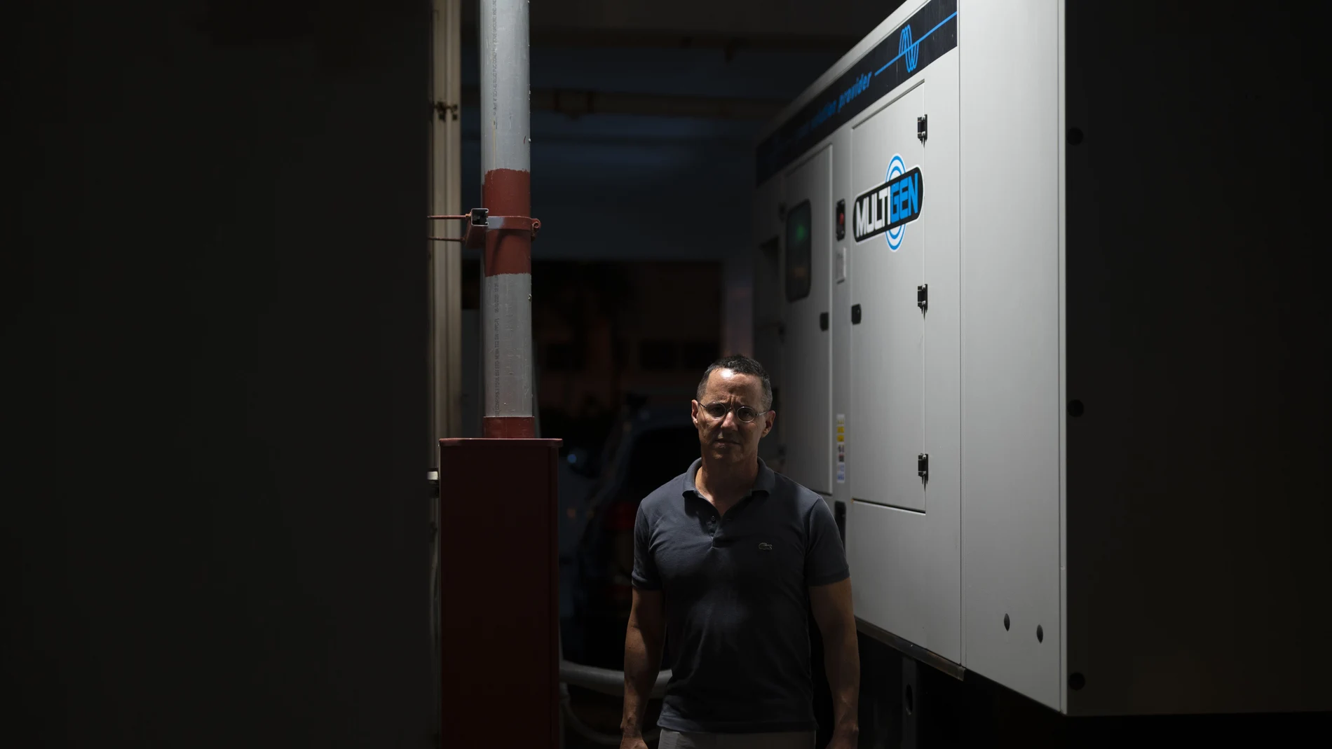 Manuel Casellas, an attorney who served as president of the Ritz condominium, poses for the camera in front of a generator bought more than a year ago at a total cost of $100,000 with the hopes that all 84 apartments could feed off it when blackouts occur, in San Juan, Puerto Rico, Thursday, Sept. 30, 2021. The residents first need a power company official to connect the generator to the grid, but officials have canceled several appointments at the last minute without explanation. (AP Photo/Carlos Giusti)