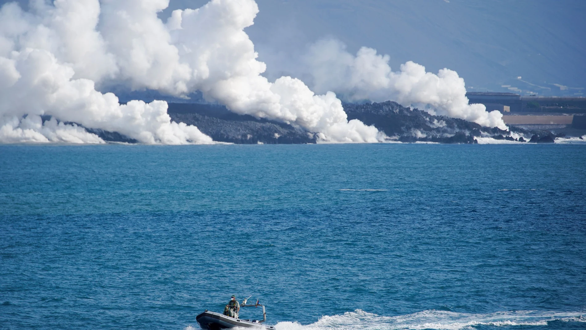 Una lancha de la Guardia Civil patrulla frente la costa, donde se aprecian las columnas de gas liberadas por la entrada en contacto de la lava con el mar