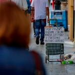Viandantes pasan junto a un cartel colocado por una persona que ejerce la mendicidad en una céntrica calle de Sevilla
