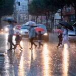 Varias personas cruzan una calle bajo la lluvia cuando el litoral sur de Valencia y norte de Alicante