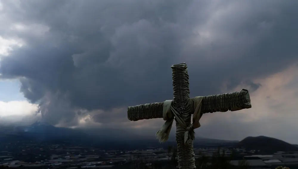 Una cruz asoma en el municipio de Los Llanos de Aridane con la nube del volcán de Cumbre Vieja al fondo