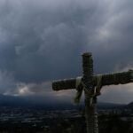 Una cruz asoma en el municipio de Los Llanos de Aridane con la nube del volcán de Cumbre Vieja al fondo