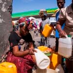 HAI01. PUERTO PRÍNCIPE (HAITÍ), 24/10/2021.- Una mujer vende gasolina en bidones y a un precio alto junto a las instalaciones de una estación de combustibles que no está prestando servicio al público hoy, en Puerto Príncipe (Haití). La acción de las decenas de bandas armadas que operan en Puerto Príncipe es una de las causas que ha dificultado el abastecimiento de combustible y ha ocasionado la escasez, que es recurrente desde hace tres meses. EFE/ Orlando Barría