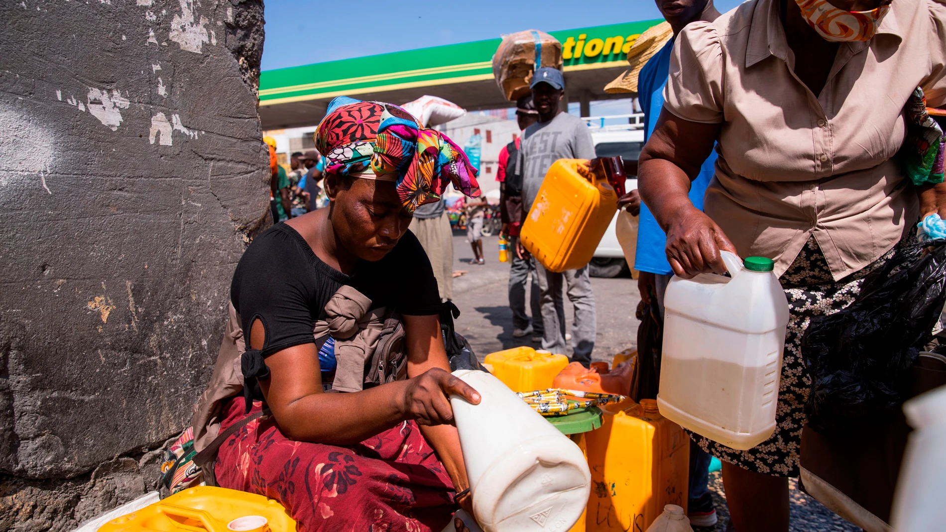 HAI01. PUERTO PRÍNCIPE (HAITÍ), 24/10/2021.- Una mujer vende gasolina en bidones y a un precio alto junto a las instalaciones de una estación de combustibles que no está prestando servicio al público hoy, en Puerto Príncipe (Haití). La acción de las decenas de bandas armadas que operan en Puerto Príncipe es una de las causas que ha dificultado el abastecimiento de combustible y ha ocasionado la escasez, que es recurrente desde hace tres meses. EFE/ Orlando Barría