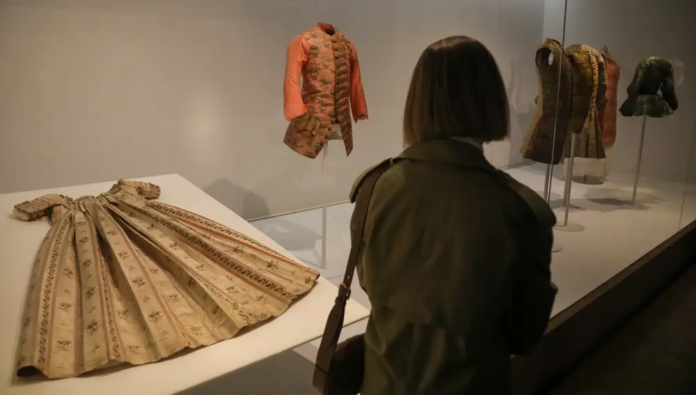 Una persona pasa por delante de algunas de las prendas de la reinauguración del Museo del Traje, a 27 de octubre de 2021, en Madrid, (España).