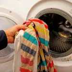 Una persona introduce ropa sucia en una lavadora