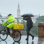 Un ciclista y un joven, cruzando el Puente de Isabel II en un día lluvioso