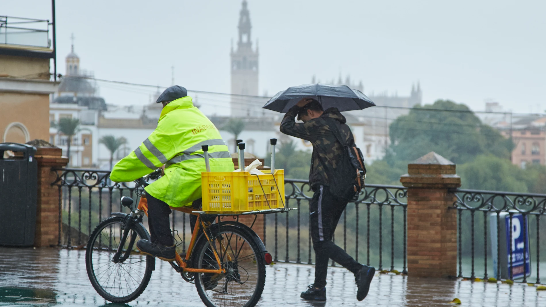 Un ciclista y un joven, cruzando el Puente de Isabel II en un día lluvioso