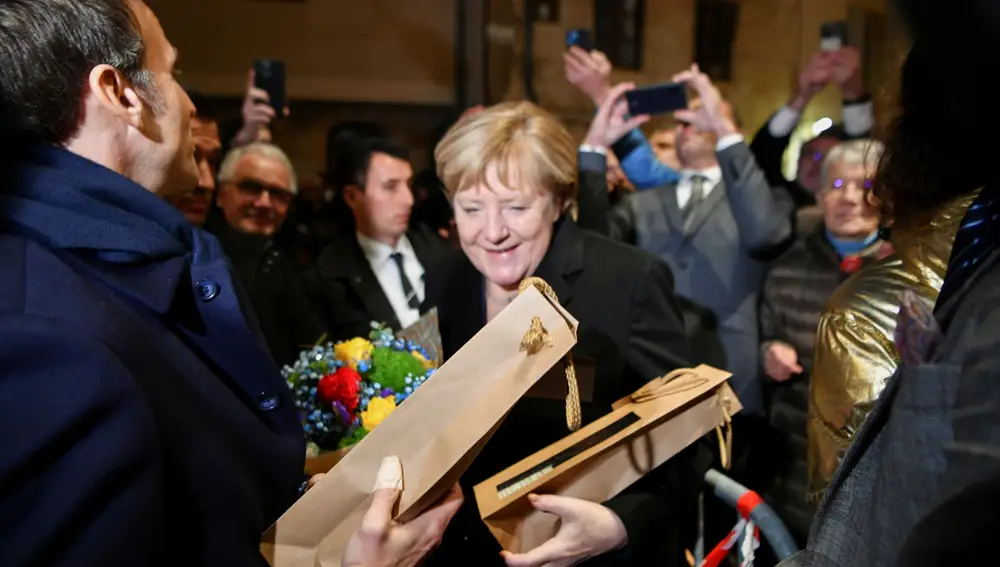 Outgoing German Chancellor Angela Merkel and France's President Emmanuel Macron receive flowers and a bottle of wine as gifts upon their arrival for talks, in Beaune, France, November 3, 2021. Philippe Desmazes/Pool via REUTERS