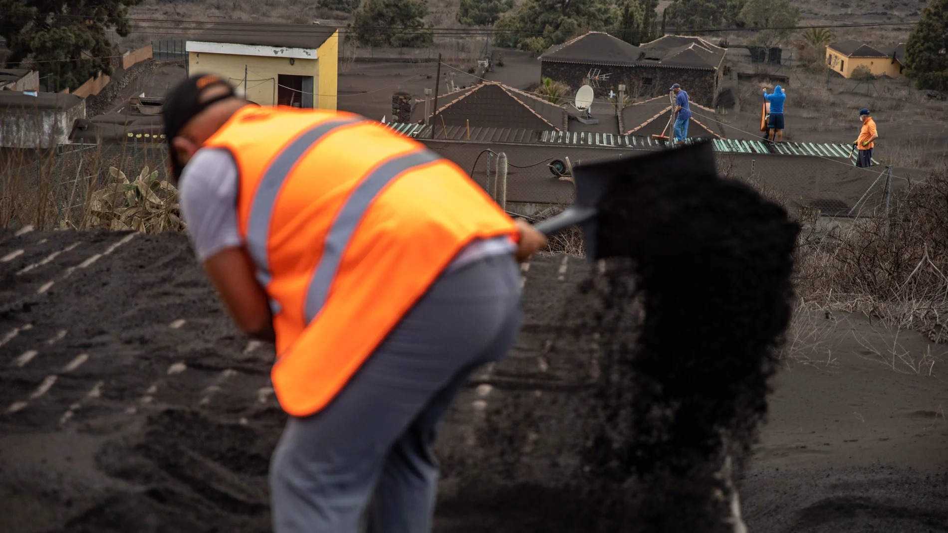 Varios voluntarios trabajan retirando cenizas de los tejados de casas próximas al volcán