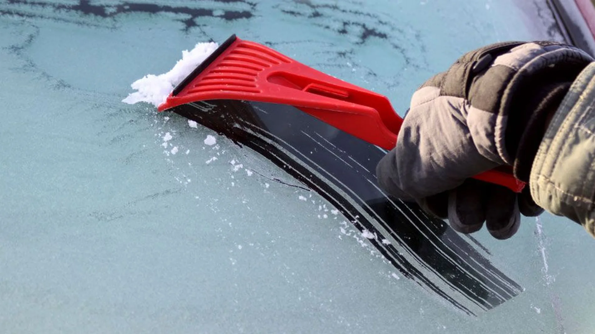 Un hombre retira hielo del parabrisas de su vehículo
