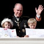El Príncipe Alberto II de Mónaco saluda mientras sus hijos, el Príncipe Jacques (d) y la Princesa Gabriella (i), sostienen mensajes. EFE / SEBASTIEN NOGIER