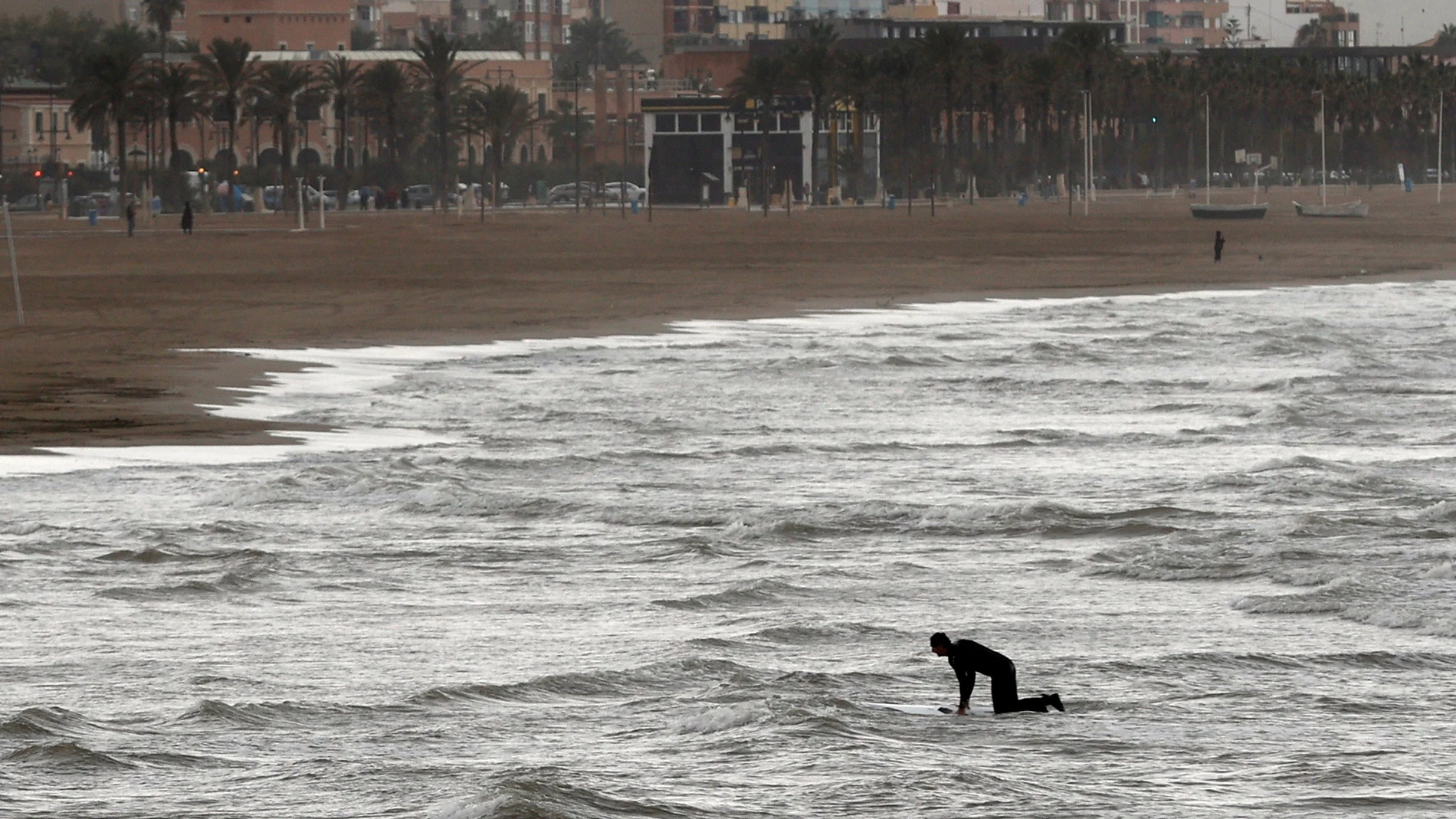 Una persona practica surf en la playa de la Malvarosa, prácticamente desierta.