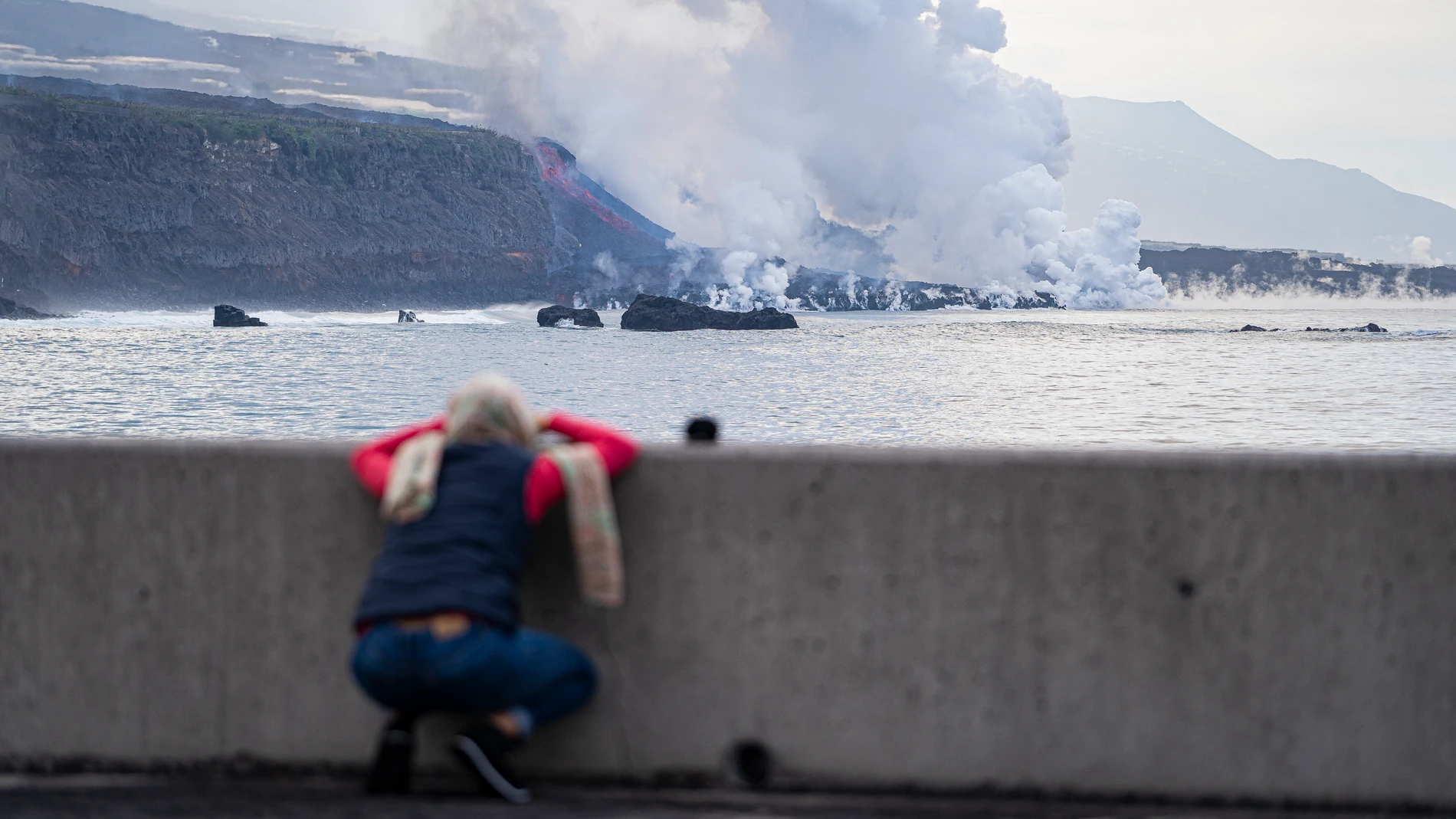 Una persona observa la colada de lava a su llegada al mar,