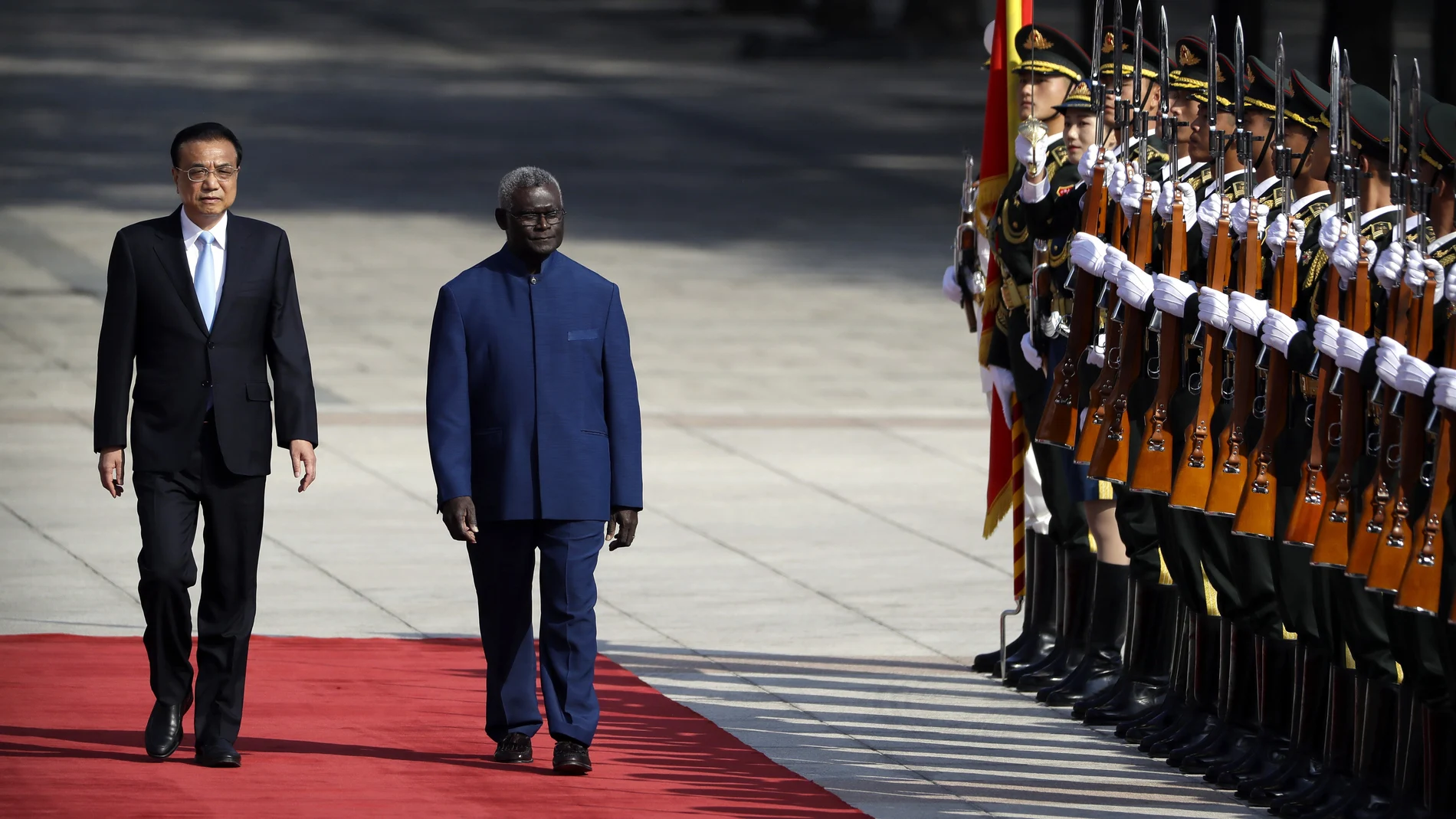 FILE - Chinese Premier Li Keqiang, left, and Solomon Islands Prime Minister Manasseh Sogavare review an honor guard during a welcome ceremony at the Great Hall of the People in Beijing, Wednesday, Oct. 9, 2019. The Solomon Islands' decision to switch its diplomatic allegiance from Taiwan to Beijing in 2019, has been blamed for arson and looting in the capital Honiara, where protesters are demanding the prime minister's resignation. (AP Photo/Mark Schiefelbein, File)