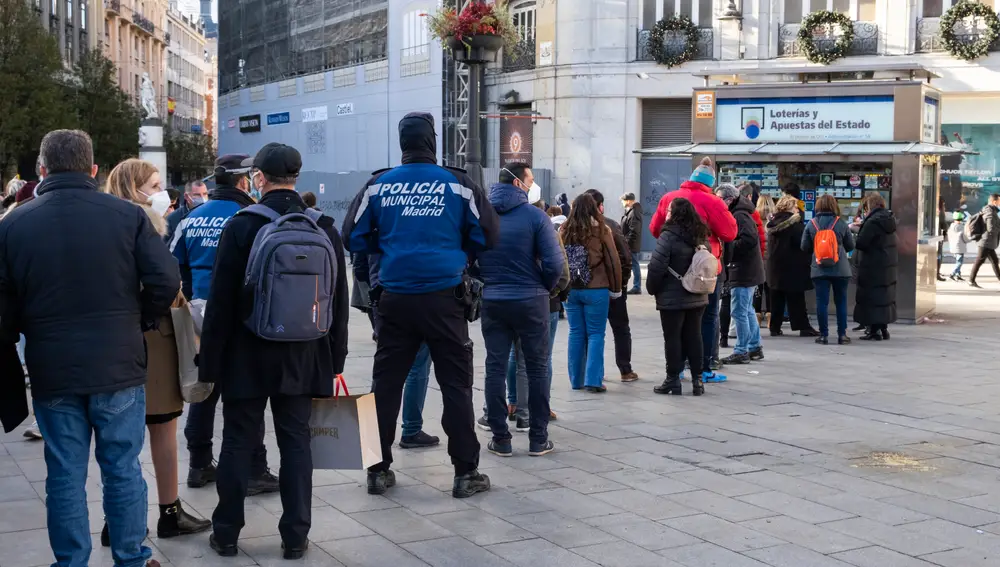 Imagen de una cola para comprar lotería en la Puerta del Sol. En ella se encuentran dos policías municipales que esperan su turno para adquirir decimos de lotería.