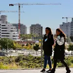 Dos jóvenes pasan por delante de varias promociones de viviendas en construcción