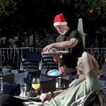 Un camarero ataviado con un gorro navideño y en manga corta, sirve una mesa a turistas que toman el sol en una céntrica terraza en Valencia