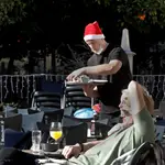 Un camarero ataviado con un gorro navideño y en manga corta, sirve una mesa a turistas que toman el sol en una céntrica terraza en Valencia