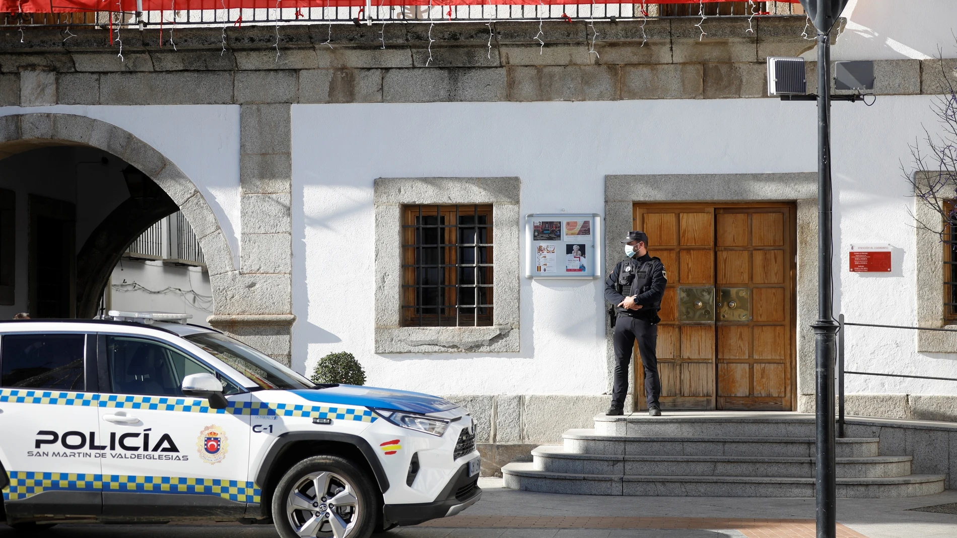 Miembros de la Policía Local d San Martín de Valdeiglesias vigilan el acceso al consistorio mientras integrantes del grupo de intervención de delitos financieros de la Guardia Civil registran la sede del Ayuntamiento