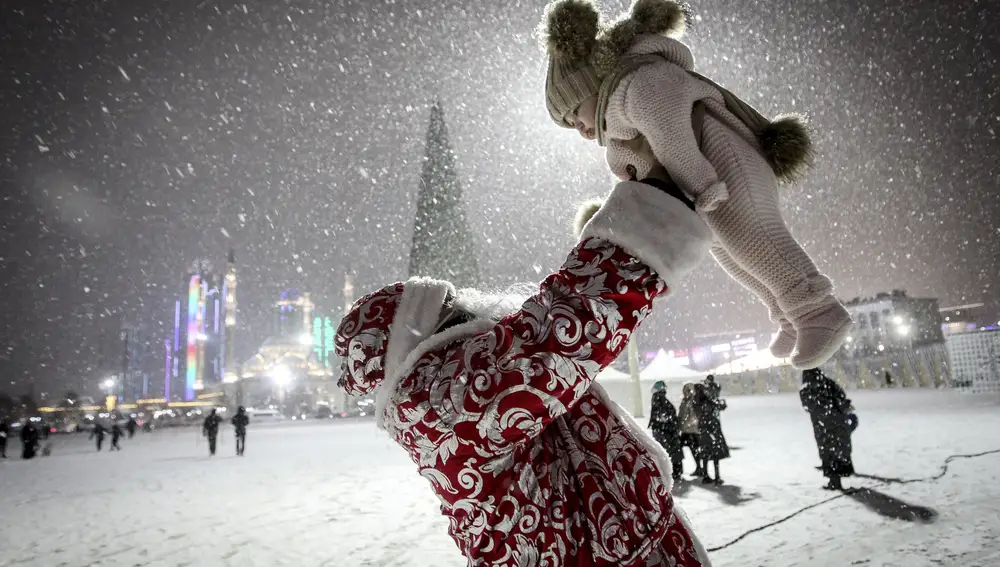 Un actor vestido como Ded Moroz juega con un niño durante la nevada en una plaza con un árbol de Navidad durante las celebraciones de Año Nuevo en Grozny, Rusia | Fuente: AP Photo / Musa Sadulayev