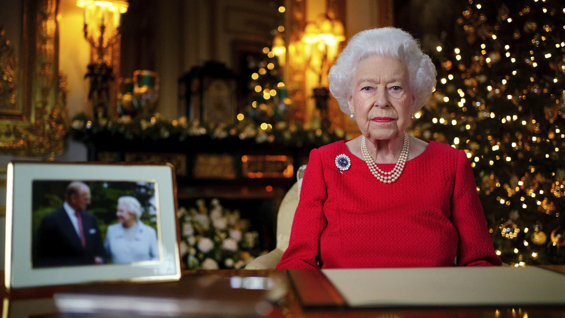 In this undated photo issued on Thursday Dec. 23, 2021, Britain's Queen Elizabeth II records her annual Christmas broadcast in Windsor Castle, Windsor, England. The photograph at left shows The Queen and Prince Philip taken in 2007 at Broadlands to mark their Diamond wedding anniversary. (Victoria Jones/Pool via AP)