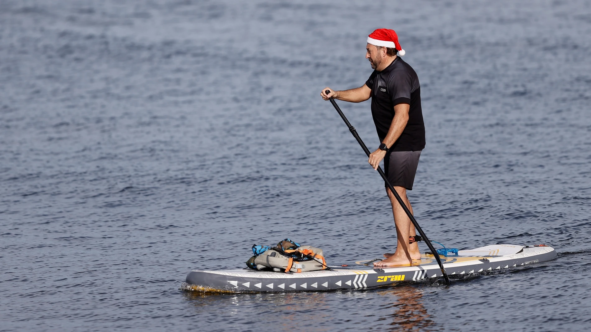 Una persona ataviada con un gorro de Papá Noel practica paddle surf en las aguas de la Malvarrosa durante la mañana de este segundo día de navidad aprovechando el buen tiempo que se vive en el litoral durante este último domingo del año