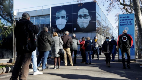 Decenas de ciudadanos guardan su turno en cola para acceder al centro de vacunación instalado en la Fira de Barcelona, hoy lunes, primer aniversario del inicio de la vacunación contra la Covid