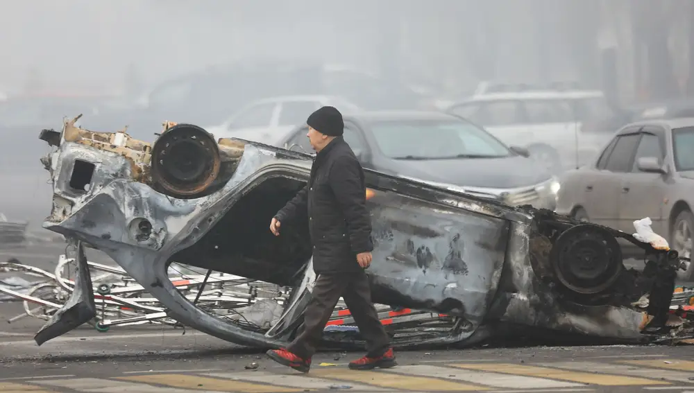 Un hombre camina frente a uno de los coches que se quemaron durante las protestas contra el aumento del precio del gas en Almaty, Kazajistán