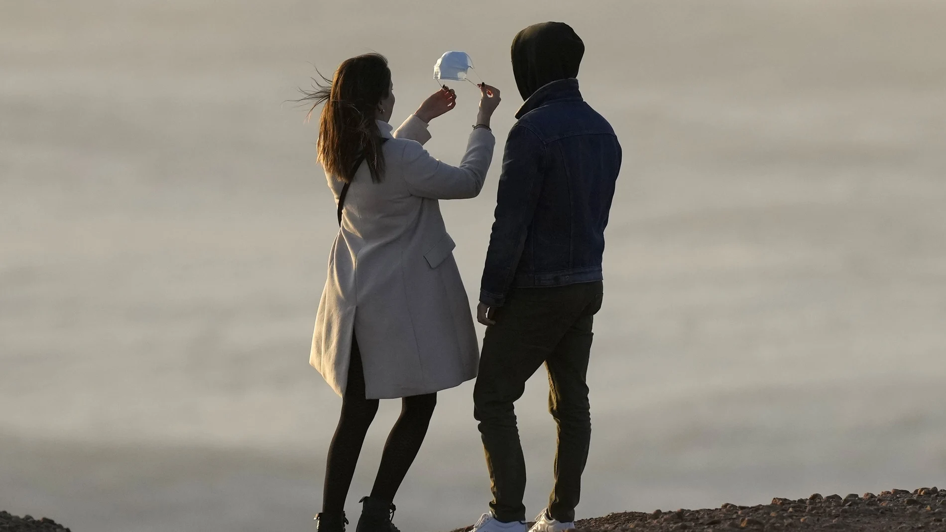 Una chica sujeta una mascarilla contra el viento en Praia do Norte (Nazaret, Portugal)